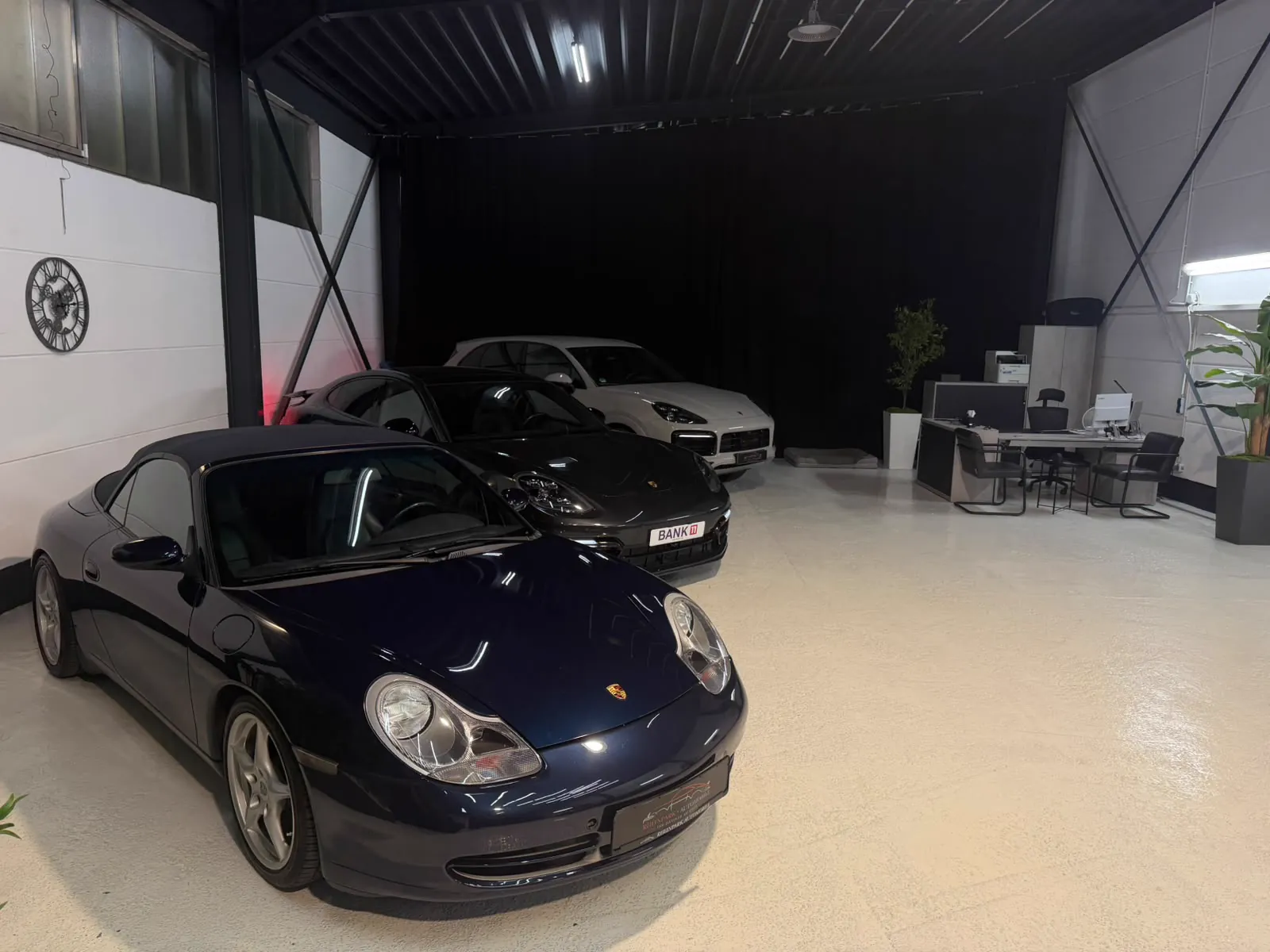 Blauer Porsche im Vordergrund mit Büro und Fahrzeugbestand